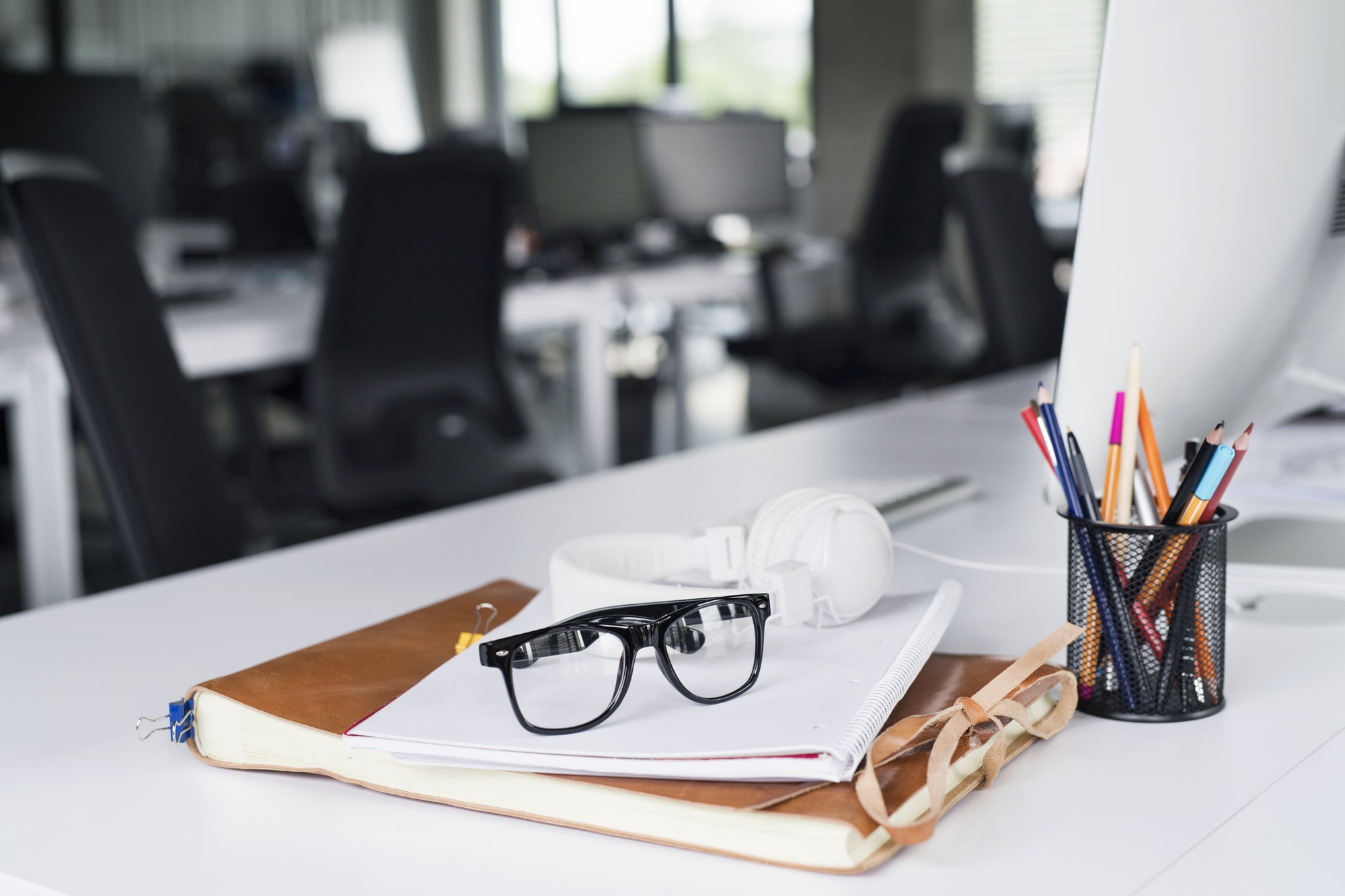 Office desk with computer, notebook and eyeglasses.
